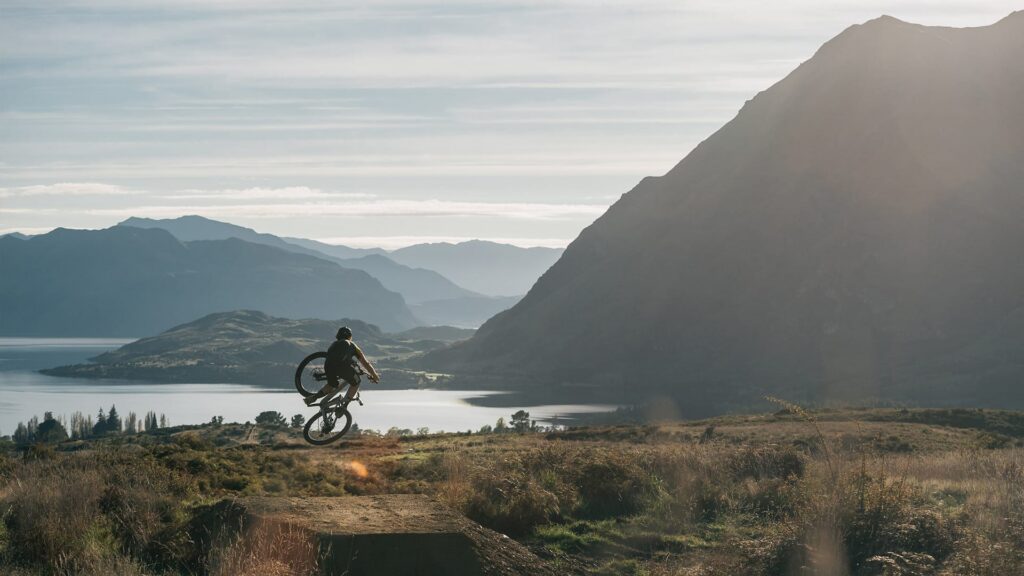 MTB rider on jump, view from Bike Glendhu in Wanaka NZ, overlooking Roy's Peak and Glendhu Bay